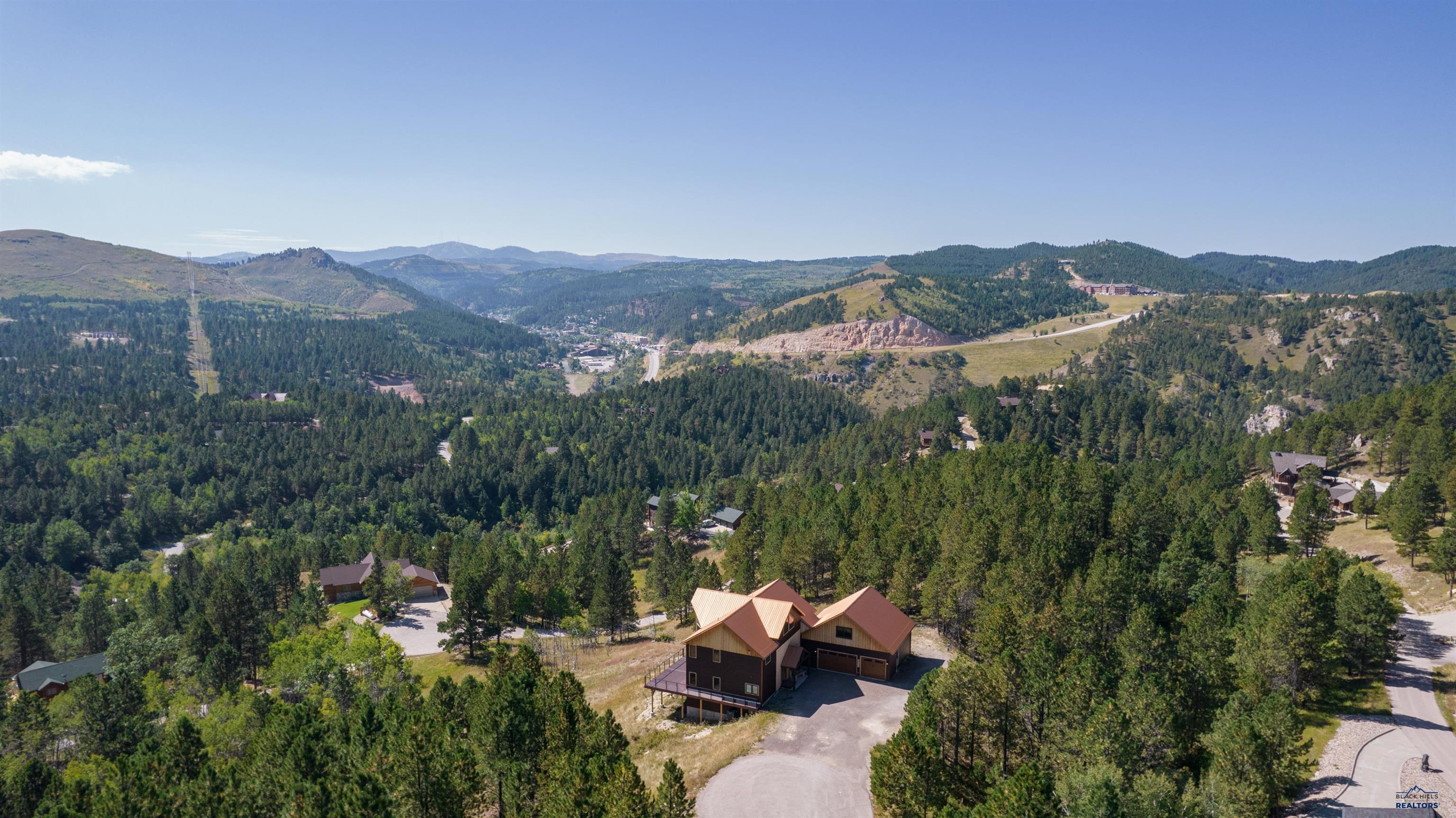 Listed by Lori Barnett, Engel & Völkers 605-786-5817.   This stunning 5-bedroom, 5.5-bathroom home is situated just minutes away from downtown Deadwood, skiing, snowmobile trails, hiking, & biking trails. Nestled on nearly 3 acres at the end of Shirt Tail Gulch, it boasts breathtaking views of the magnificent Black Hills, making it an ideal vacation home, investment property, or permanent residence.  The main level features the master, well appointed kitchen, & great room, which has impressive, two-story views. Upstairs, there is a sizable living room, two large bedrooms with ensuite bathrooms. Downstairs, you'll find a family room, plumbed for a wet bar, and two additional bedrooms, both of which also have ensuite bathrooms.  Enjoy the brand-new, enormous deck with a hot tub as you take in the panoramic views of Deadwood. This property also includes an oversized three-car garage with an extra storage room above it that could be used as a bunkhouse. Currently a nightly rental.