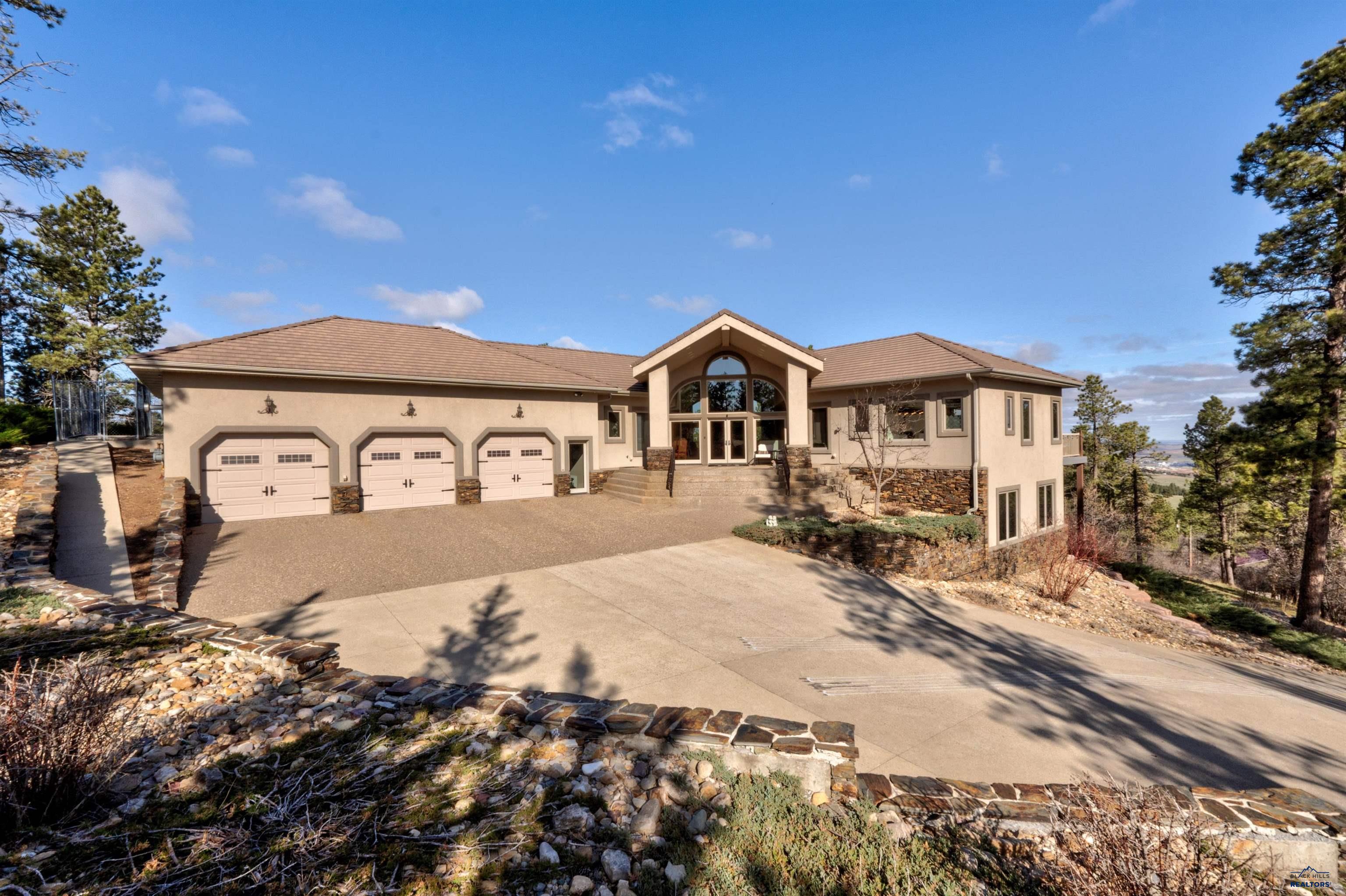 This awe inspiring property features intricate architecture with views of Spearfish. Just through the impressive glass front doors are the open living areas that feature vaulted ceilings, tall stone fireplace, extravagant windows with immaculate views & natural light. The kitchen is a culinary dream with expansive granite counter space, a prep sink, island, pantry, hardwood cabinetry, and high end appliances. Off the living room is the wrap around deck that provides views of this incredible property with natural rocks and low maintenance landscaping. The main level features a large primary bedroom with 2 walk-in closets and a stunning bathroom that is sure to impress, a dedicated office with built-in shelving and patio access, a full bathroom, and laundry area. The lower level has 3 large bedrooms, 2 full bathrooms, a multipurpose room, which is an entertainer's dream and includes a wet bar, short throw projector/screen, game room, and an additional room to use as your heart desires.