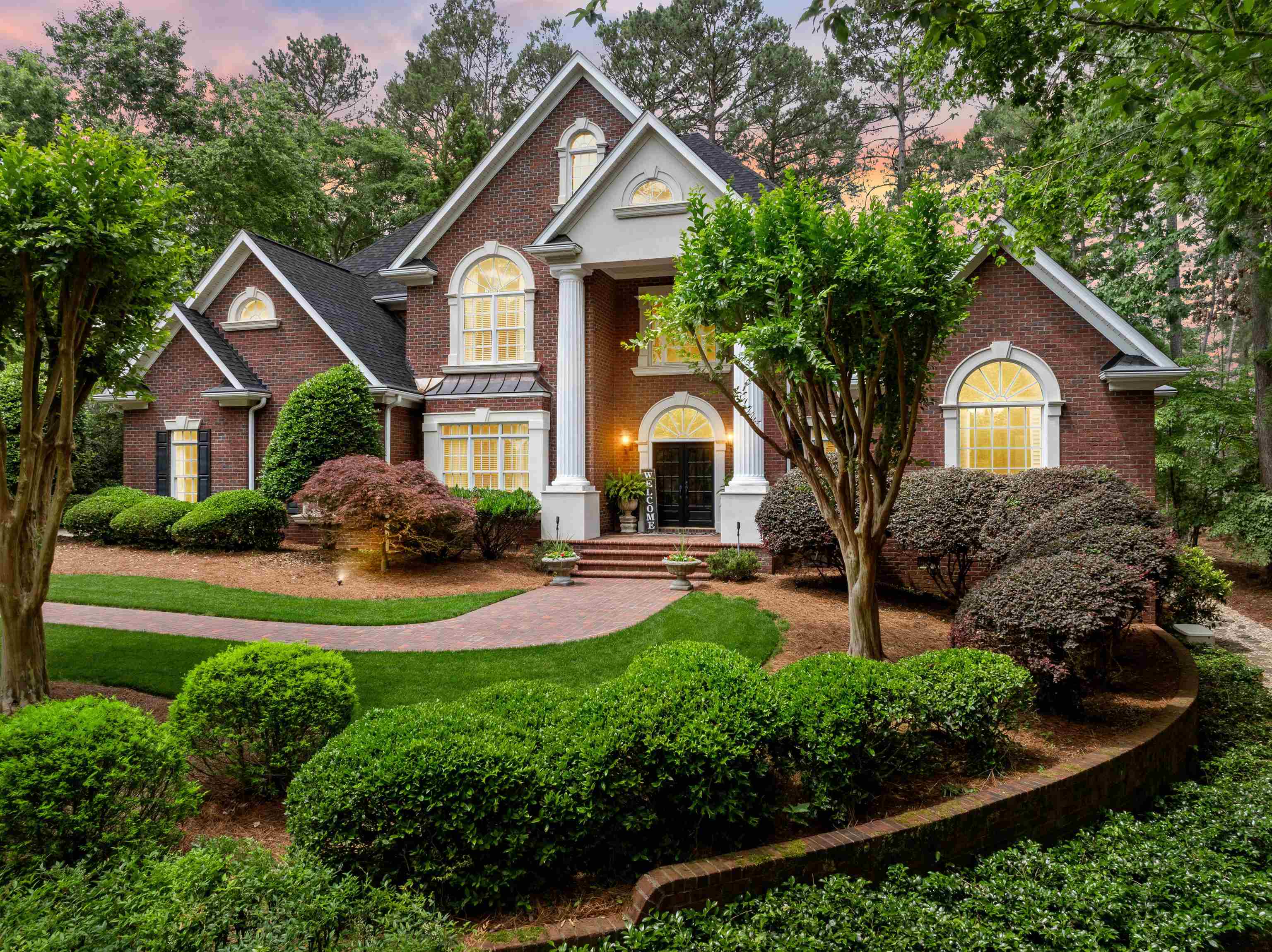 Executive Estate on the 12th Hole – 458 Carolina Drive is located in Carolina Country Club.  Come and discover the timeless elegance and unmatched golf course living at 458 Carolina Drive, a luxury brick home.  This estate is perfectly situated on the 12th hole, Par 3, of the prestigious Carolina Country Club. This premium homesite offers direct backyard access to the green, allowing you to step out your door and enjoy the beauty and serenity of course-side living. From the winding driveway with extra parking to the grand columned entry and professionally designed landscaping, this home makes a striking first impression. Inside, the two-story foyer welcomes you with a sweeping staircase, wrought-iron rails, and a bridge overlooking the family room and fairway. The living room currently is used as a dining room features a gas fireplace, custom built-ins, and rich trim details. A butler’s pantry connects the dining seamlessly to the chef’s kitchen, complete with double ovens, gas cooktop island, warming drawer, desk area, and extensive cabinetry. The family room boasts soaring ceilings, a stone-framed wood-burning fireplace, and floor-to-ceiling windows with views of the golf course, patio and the pond with 2 waterfalls.  The main-level primary suite is a private retreat with a sitting room, vaulted and tray ceilings. The spa-like ensuite includes a jetted tub, double walk-in shower, dual vanities, and two spacious walk-in closets. Upstairs are three generous bedrooms, each with en suite bathrooms and walk-in closets, plus a loft area with front and rear views of the lawn. A private  suite off the kitchen features a kitchenette, full bath, and flex space. Additional features include: * Generac whole-home generator (natural gas, automatic transfer switch) * Covered patio with wood ceiling, brick columns, and wood-burning fireplace * Stone and stamped concrete walkways with built-in seating and water views * Detached two-car garage with finished flex room above. * Laundry chute in one bedroom for ease of dropping directly to the laundry room * Professionally landscaped yard with boulders, stone steps, and multiple paths to enjoy the setting Residents have the option to join Carolina Country Club’s golf, athletic, social, or corporate memberships. The community features a Tom Jackson-designed 18-hole championship course, practice facilities, clubhouse, tennis, fitness center, and social calendar. This course is considered one of the finest in the Upstate, with scenic water features, streams, lakes, and a layout suitable for all skill levels.
