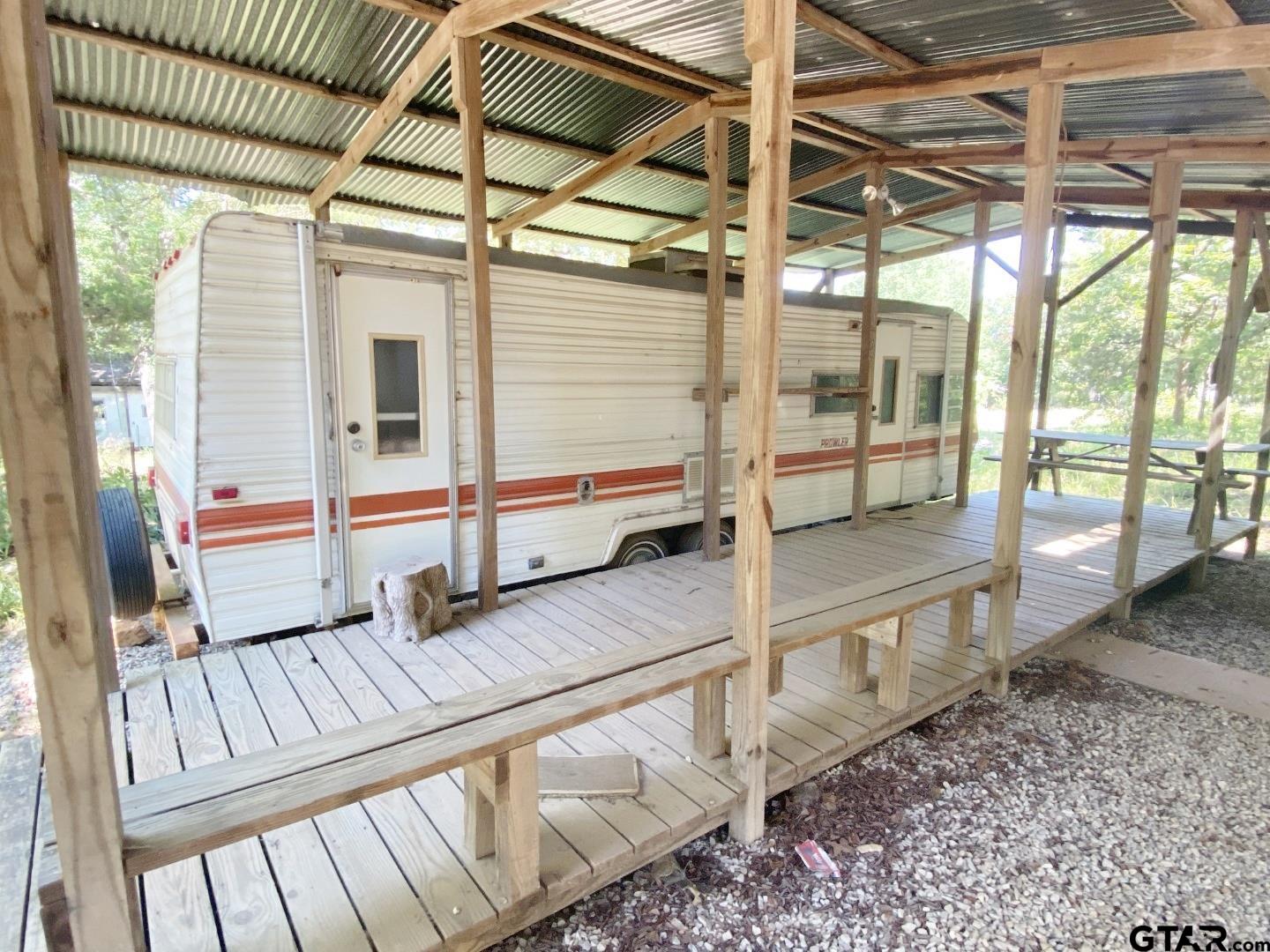 A covered wooden deck leads you up to a cozy Prowler camper with all living amenities inside.