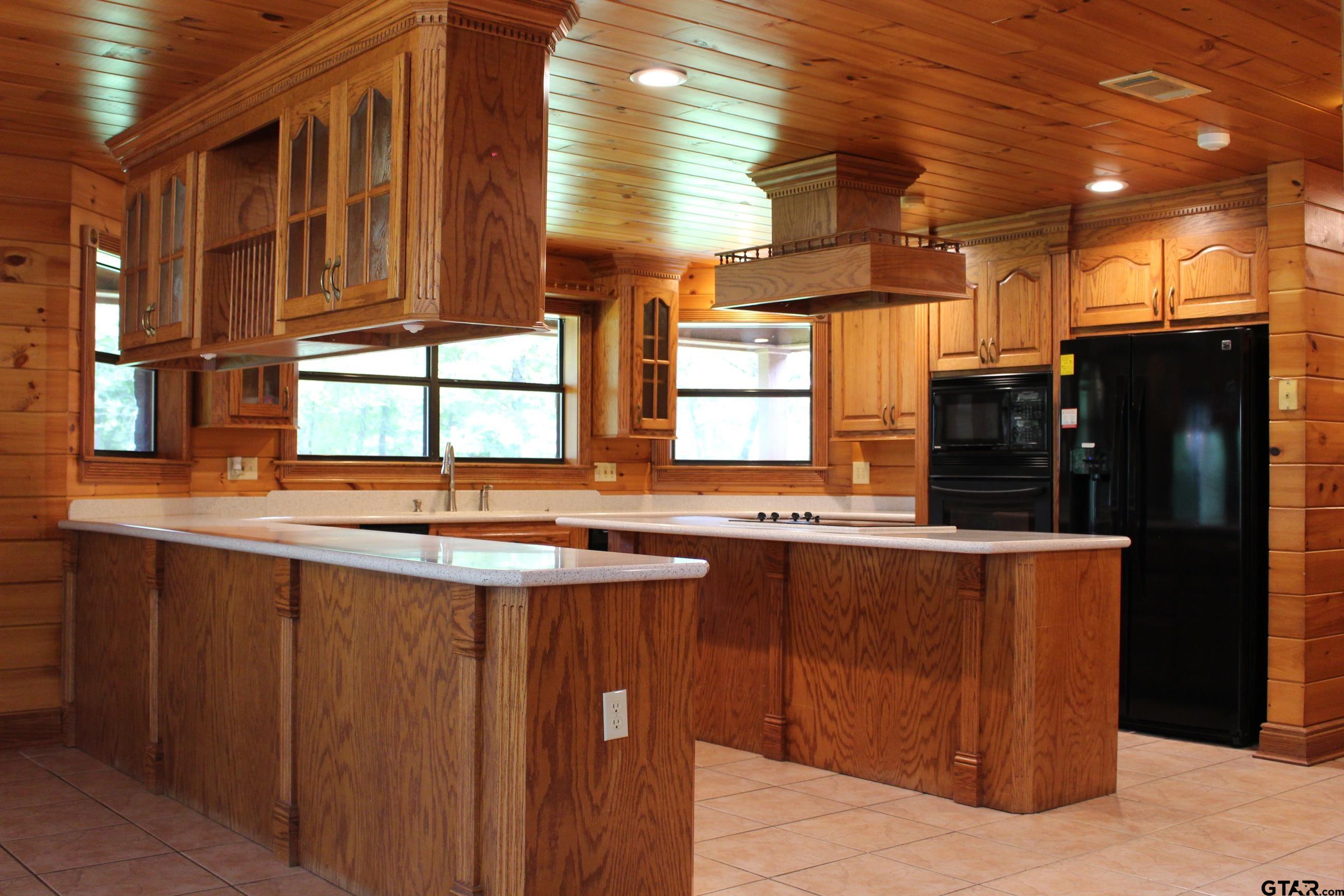 Kitchen with black appliances, light tile patterned floors, wooden walls and kitchen peninsula.